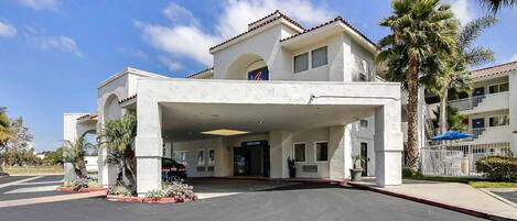 A hotel entrance with a covered driveway, palm trees, and a clear blue sky.