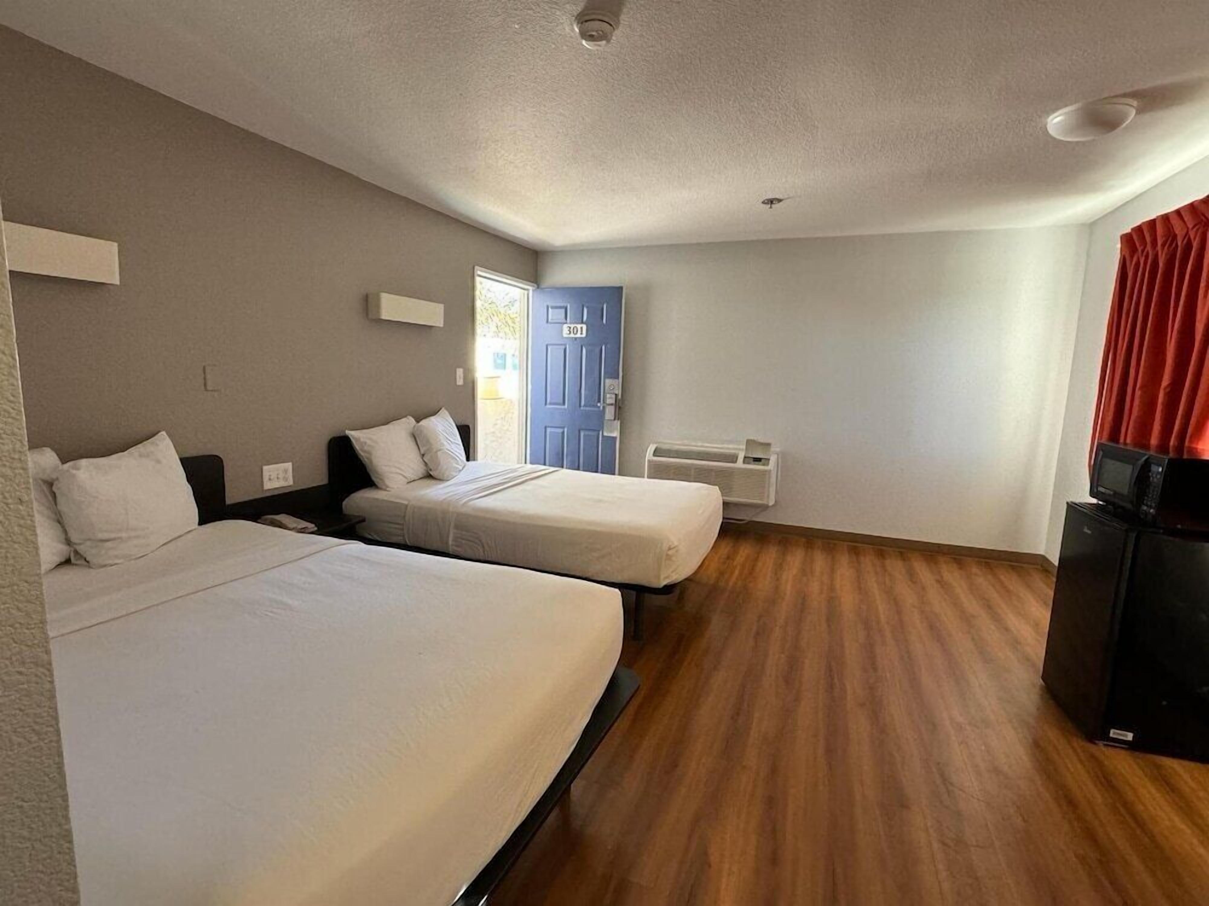 Una habitación de hotel con dos camas, una puerta, un ventanal, un calentador y un televisor.