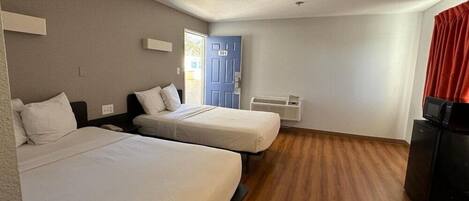 Una habitación de hotel con dos camas, una puerta, un ventanal, un calentador y un televisor.