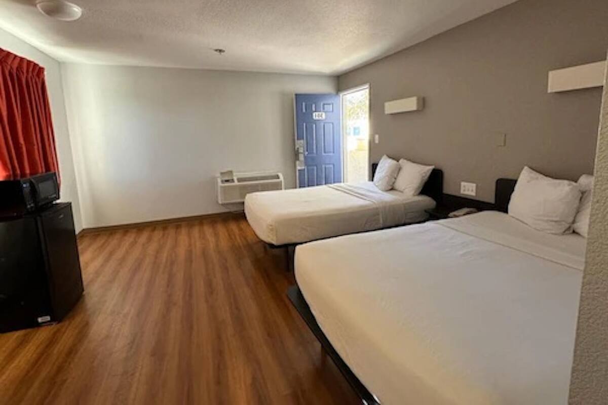 Een kamer met twee bedden, een televisie op een standaard, een deur en een raam.