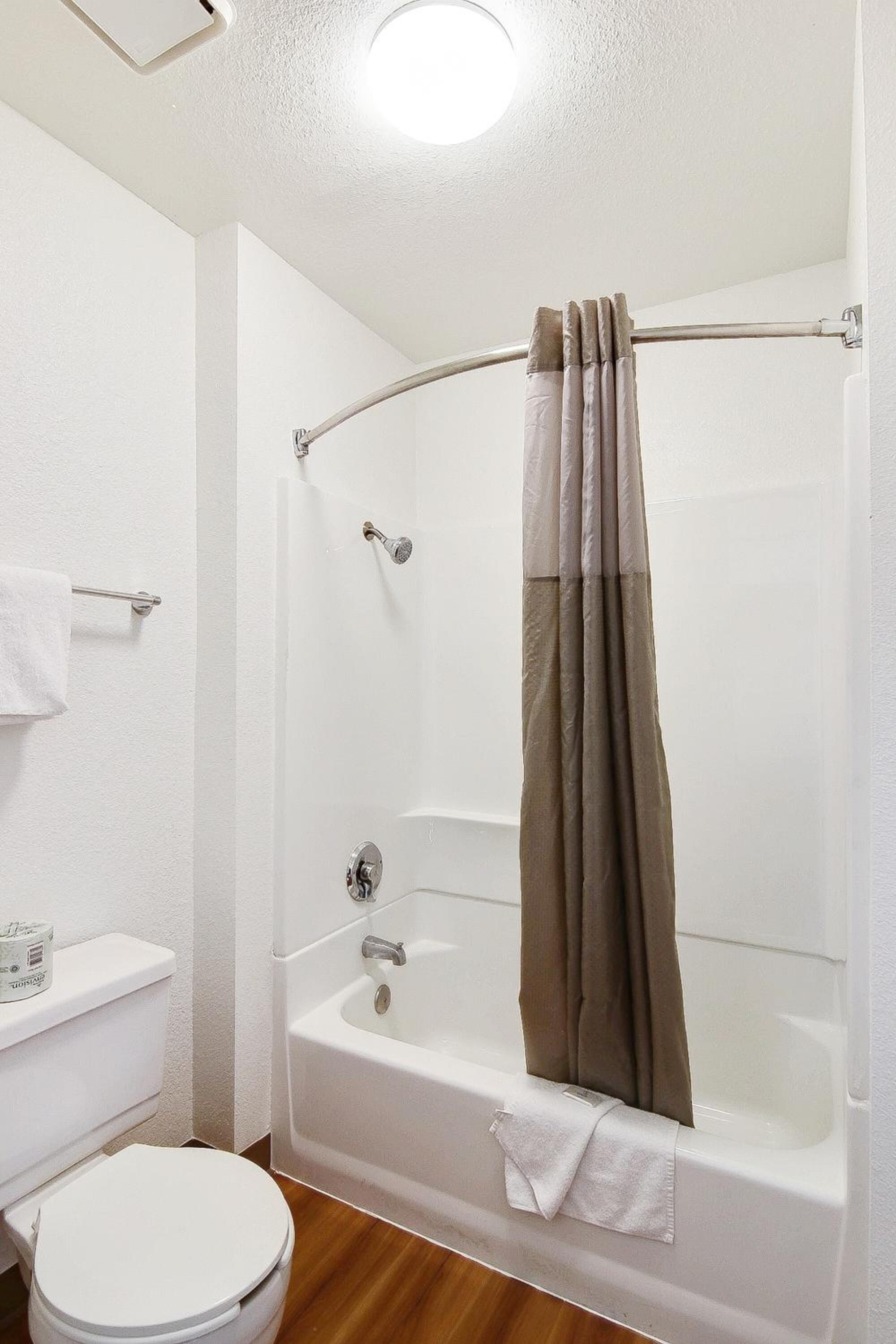 Un baño con inodoro blanco, bañera con cortina de ducha y un perchero para toallas.