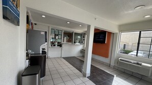 A clean, well-lit indoor space with a reception desk, a counter, and a window with a view of the outside. - Motel 6 Bellflower, CA - Los Angeles (Bellflower)