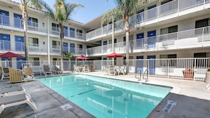 A hotel with a pool area, multiple balconies, and outdoor seating. - Motel 6 Bellflower, CA - Los Angeles (Bellflower)