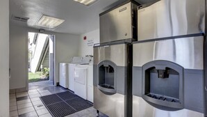 A laundry facility with a washing machine, dryers, and a ventilation system. - Motel 6 Bellflower, CA - Los Angeles (Bellflower)