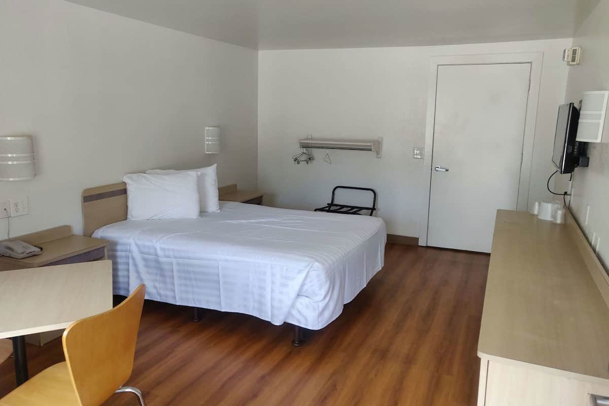 A hotel room with a bed, a desk, a chair, a wardrobe, a radiator, and a door.