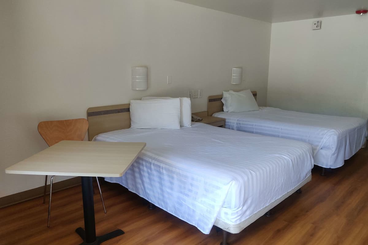 A hotel room with two beds, a small table, and a chair.