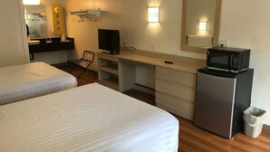 Hotelkamer met twee bedden, een bureau met een televisie, een magnetron en een kleine prullenbak.