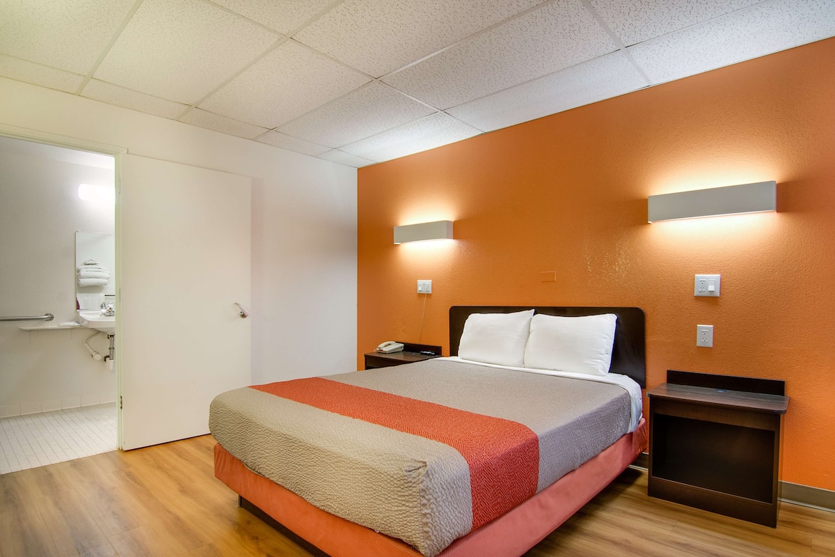 A hotel room with a bed, nightstands, a wall-mounted light, and a door leading to a bathroom.