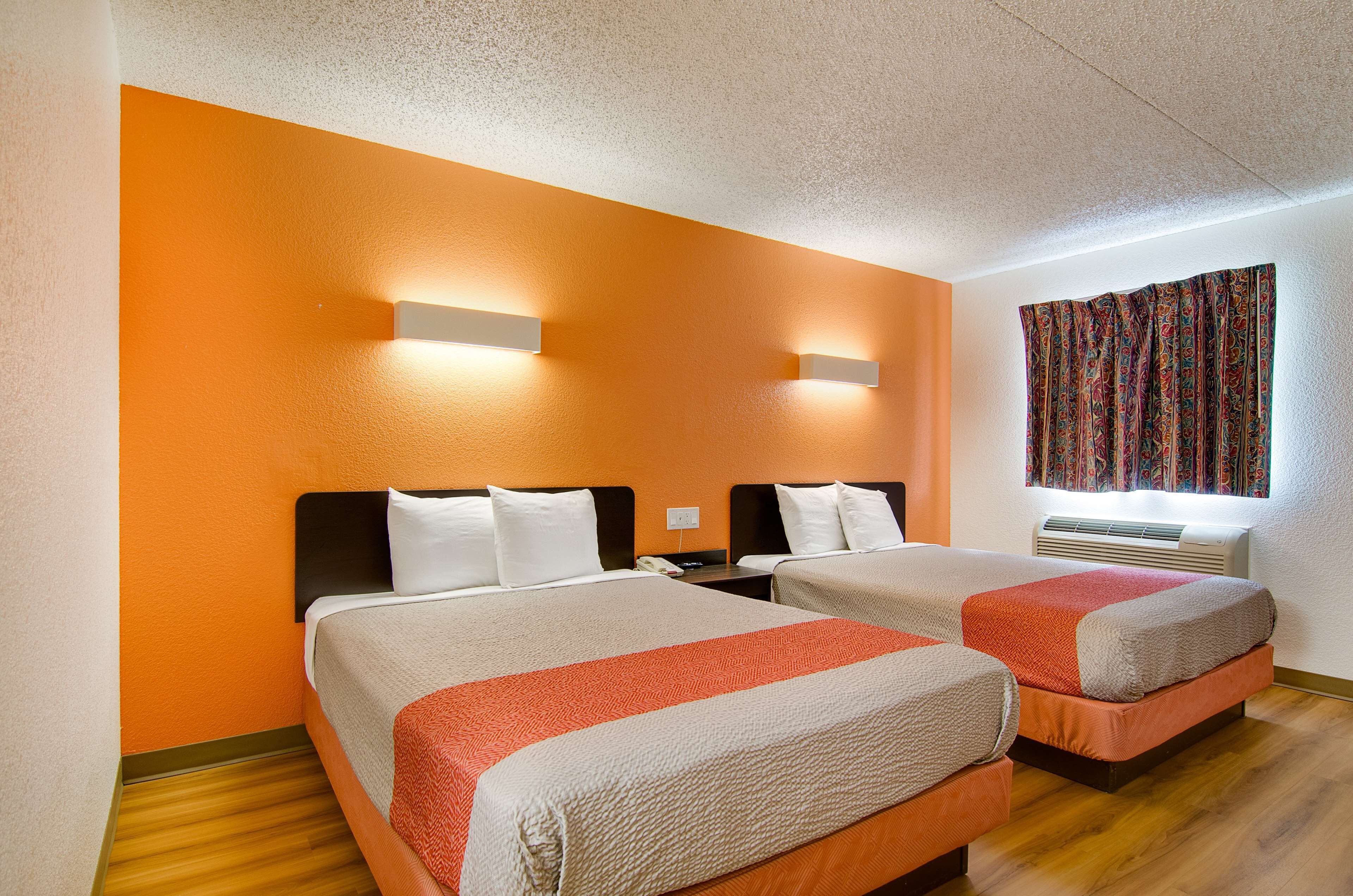 A hotel room with two beds, orange walls, and a window with patterned curtains.