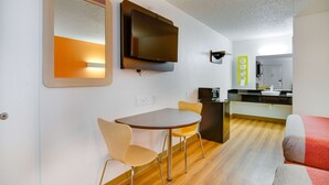 Un espacio habitable compacto con comedor, televisor de pantalla plana en la pared, kitchenette y sofá.