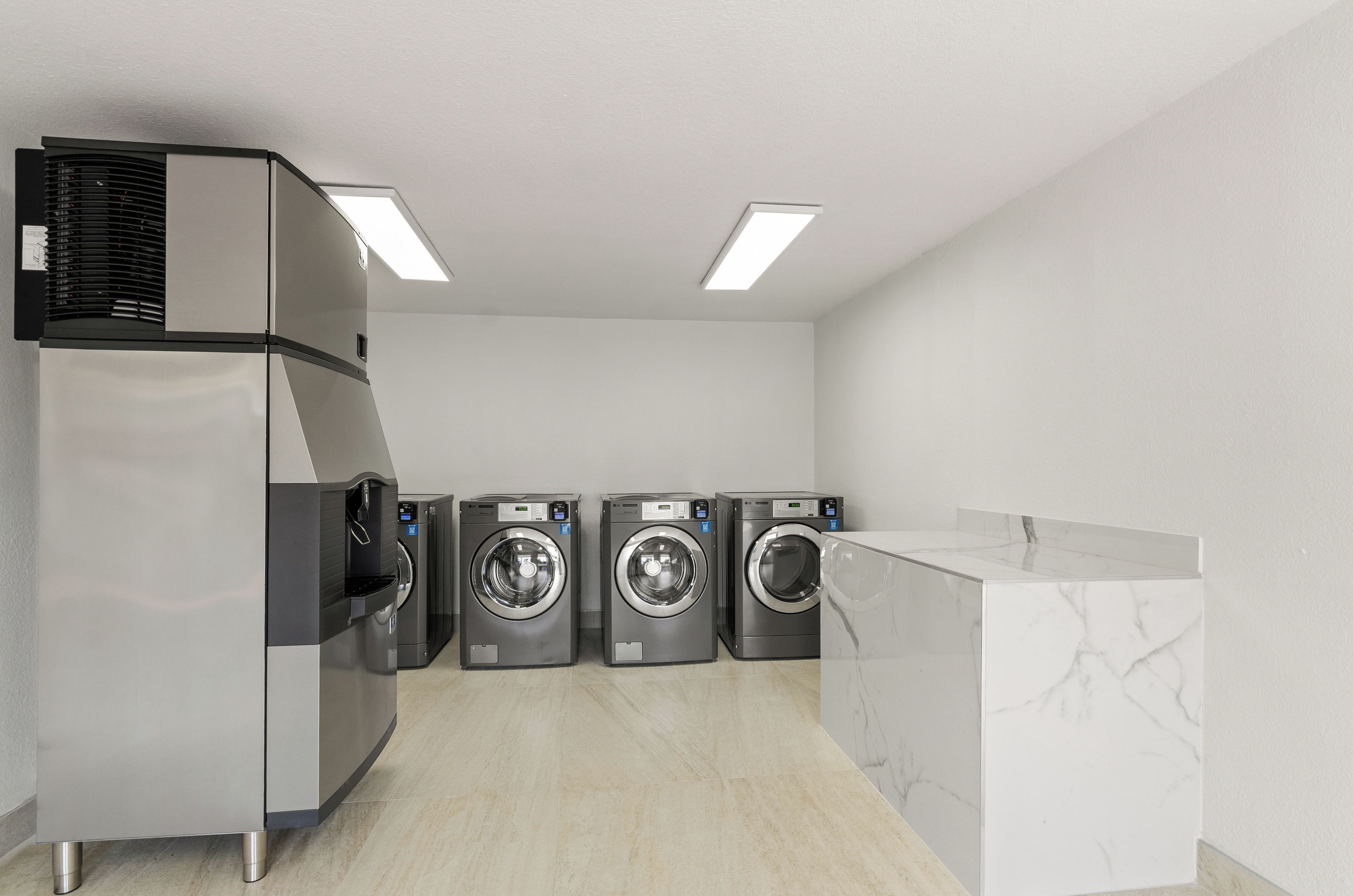 Une buanderie équipée d’un grand sèche-linge industriel, de trois machines à laver à chargement frontal et d’un comptoir en marbre.