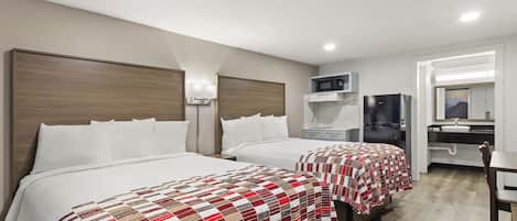 A hotel room with two beds, a desk, a refrigerator, and a bathroom.