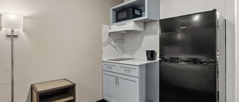 A compact kitchen with a built-in microwave, a black refrigerator, and a small wooden side table.