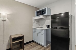 Una cocina compacta con microondas integrado, un refrigerador negro y un pequeño taburete de madera.
