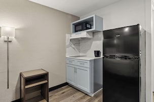 Una cocina compacta con microondas integrado, un refrigerador negro y un pequeño taburete de madera.