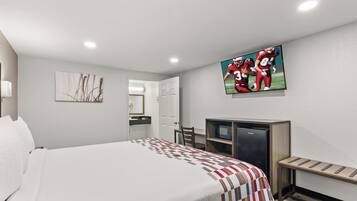 A hotel room with a bed, a television mounted on the wall, a desk with a microwave, and a door leading to a bathroom.