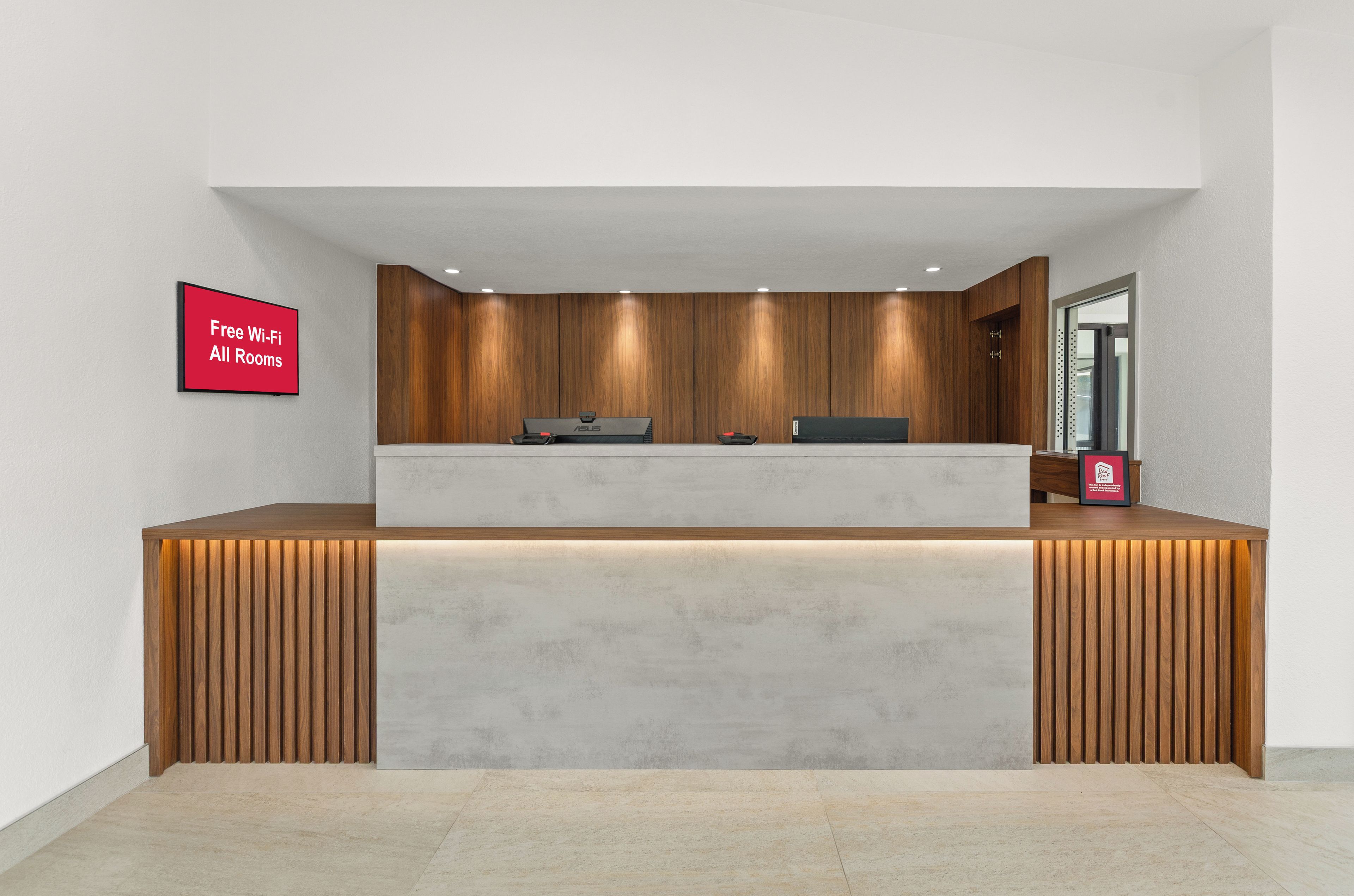 A reception desk with a wooden panel backdrop, a flat-screen TV, and a sign indicating free Wi-Fi and all rooms.