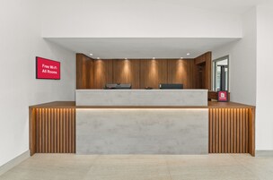 Un mostrador de recepción con un panel de madera de fondo, un televisor de pantalla plana y un cartel que indica Wi-Fi gratuito y habitaciones disponibles.
