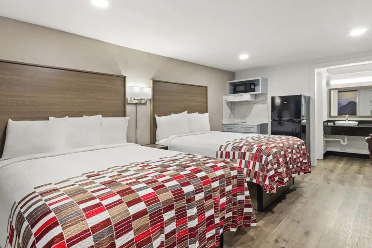 Una habitación de hotel con dos camas, microondas, refrigerador, lavamanos y espejo.