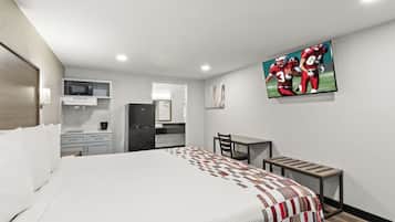 Une chambre d’hôtel équipée d’un lit, d’un bureau, d’une chaise, d’un four à micro-ondes, d’un réfrigérateur et d’un téléviseur fixé au mur.