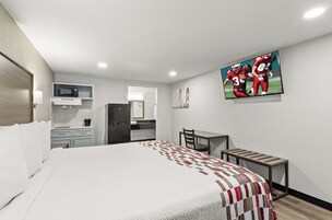 Habitación de hotel con cama, escritorio, silla, microondas, refrigerador y televisión montada en la pared.