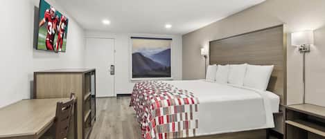A hotel room with a bed, a desk, a chair, a painting on the wall, and a lamp.