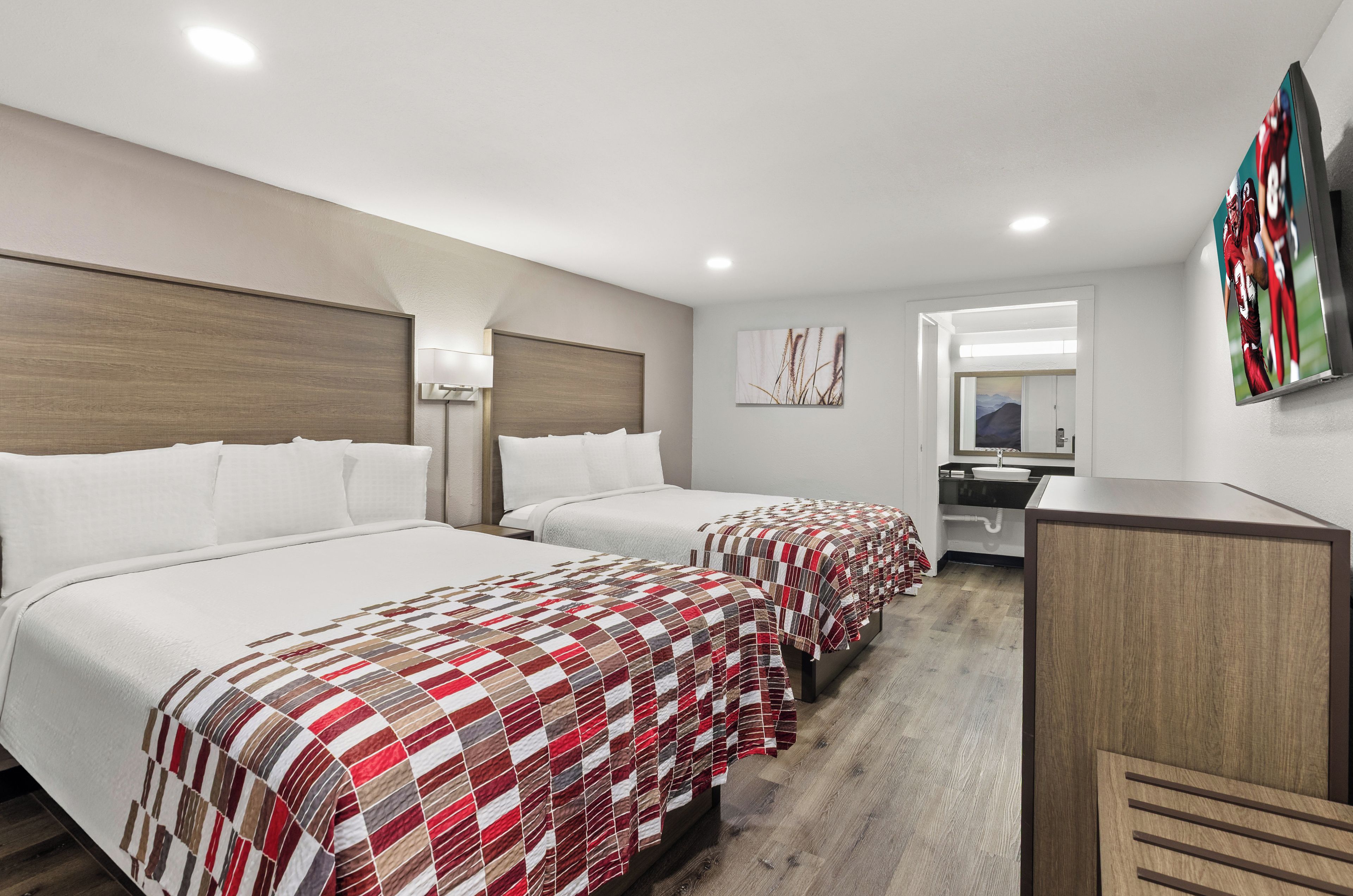 Habitación de hotel con dos camas, un escritorio, un espejo y un televisor en la pared.