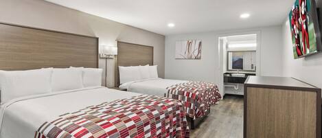 Habitación de hotel con dos camas, un escritorio, un espejo y un televisor en la pared.