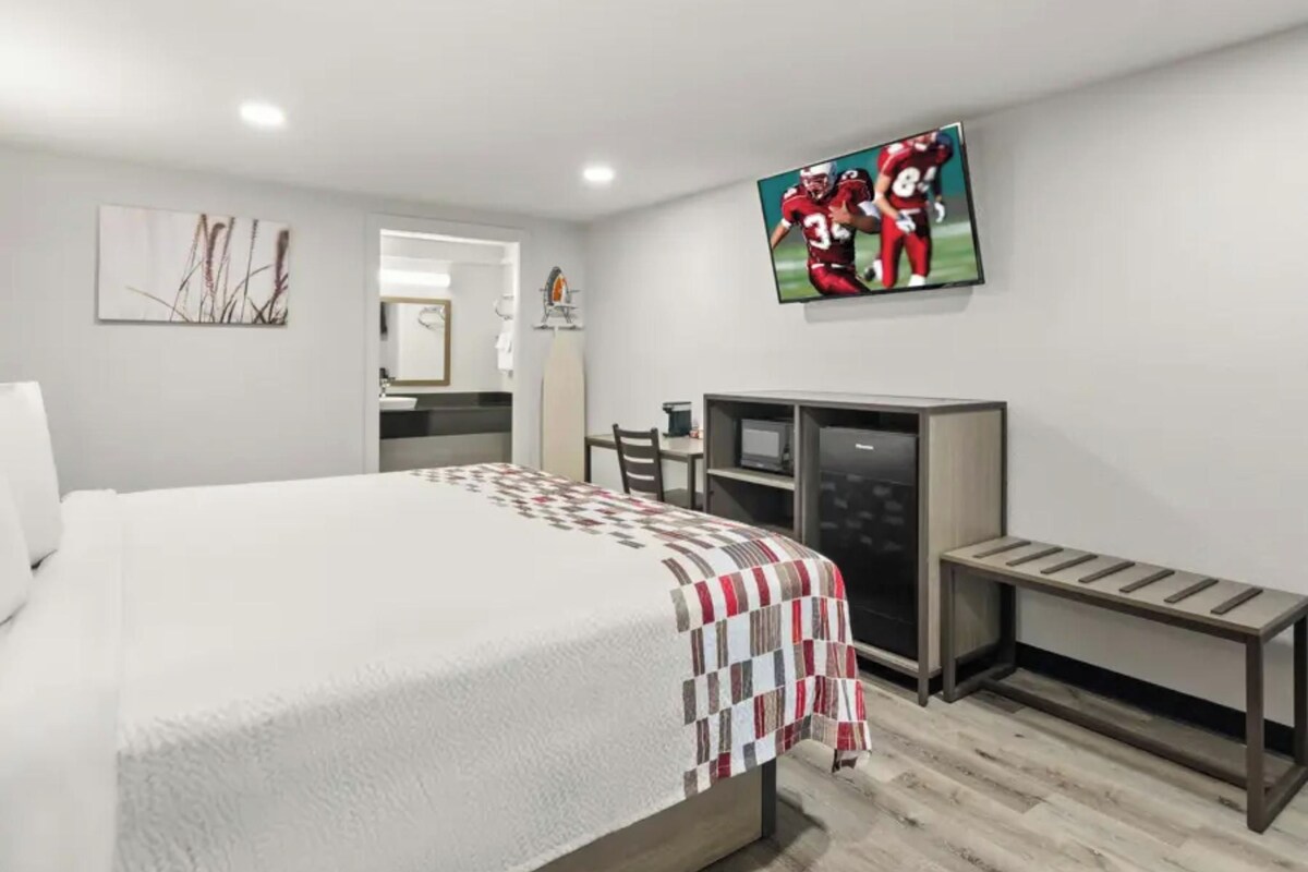 Una habitación de hotel con una cama, un escritorio, un televisor y un espejo.