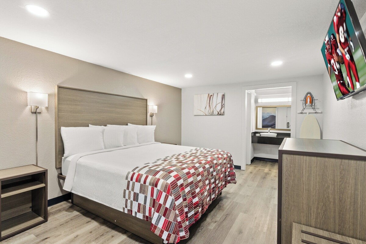 A hotel room with a large bed, bedside lamps, a mirror, a TV, and a small desk.