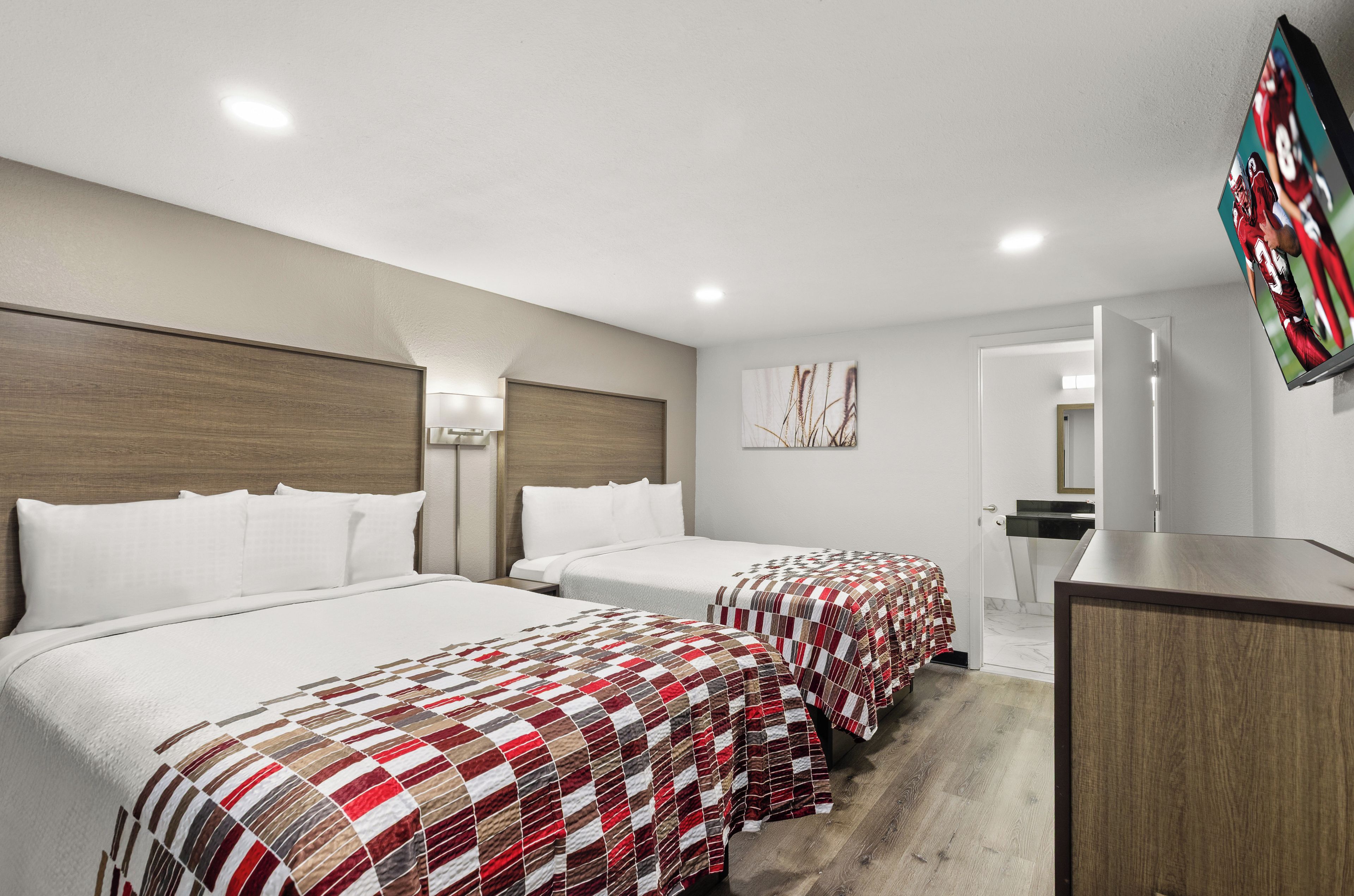 A hotel room with two beds, a desk, a mirror, and a television.