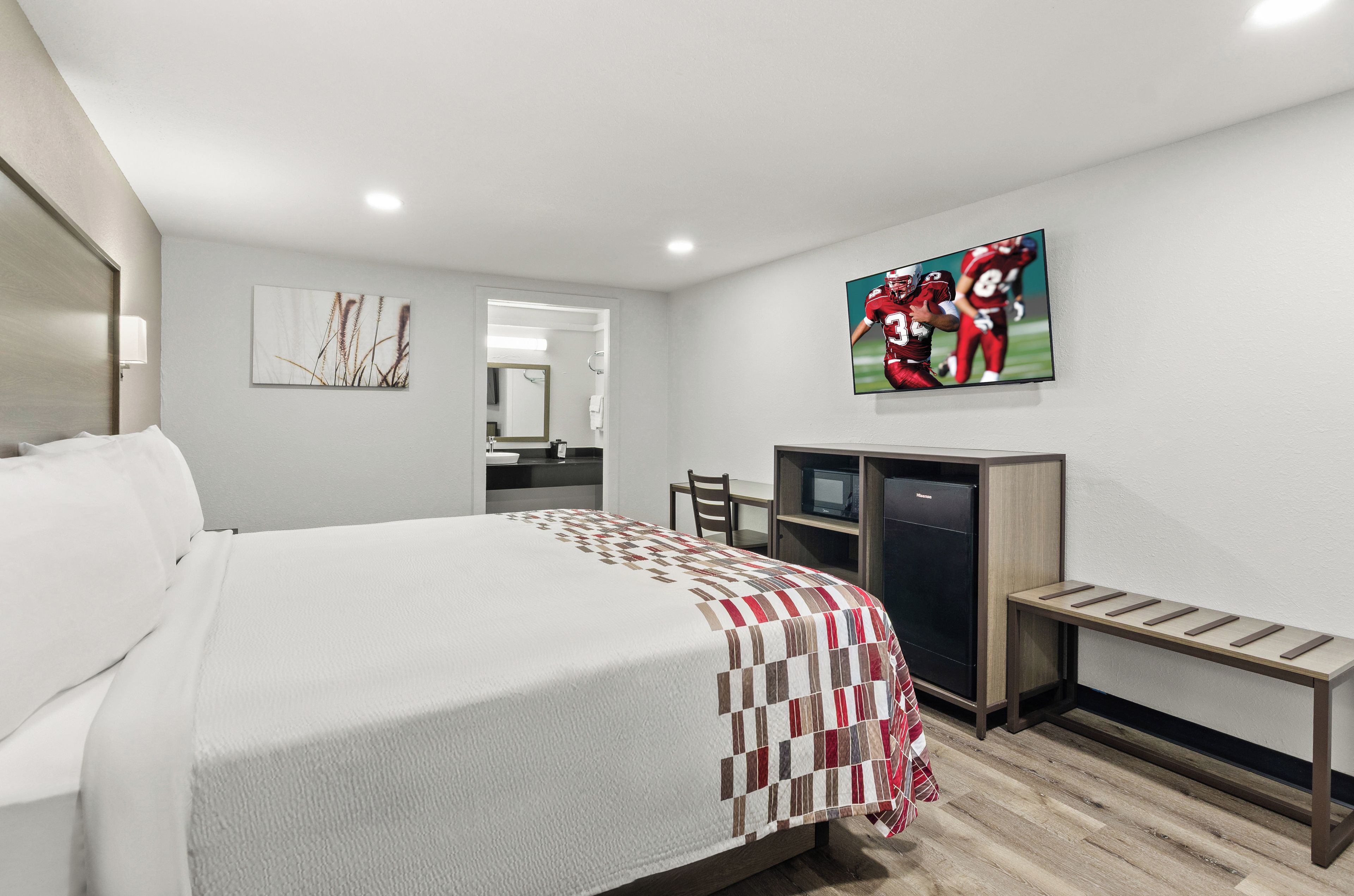 A hotel room with a bed, a desk, a television, and a mirror.