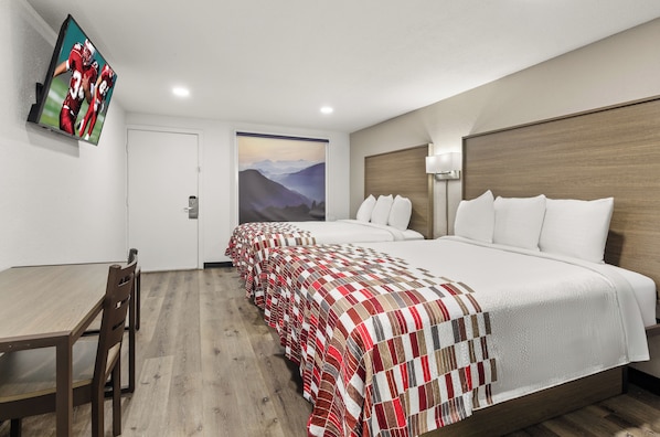 Habitación de hotel con cama, escritorio, silla, televisor montado en la pared y un cuadro.