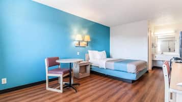 A hotel room with a bed, a desk, a chair, a small table, and a wall-mounted lamp.