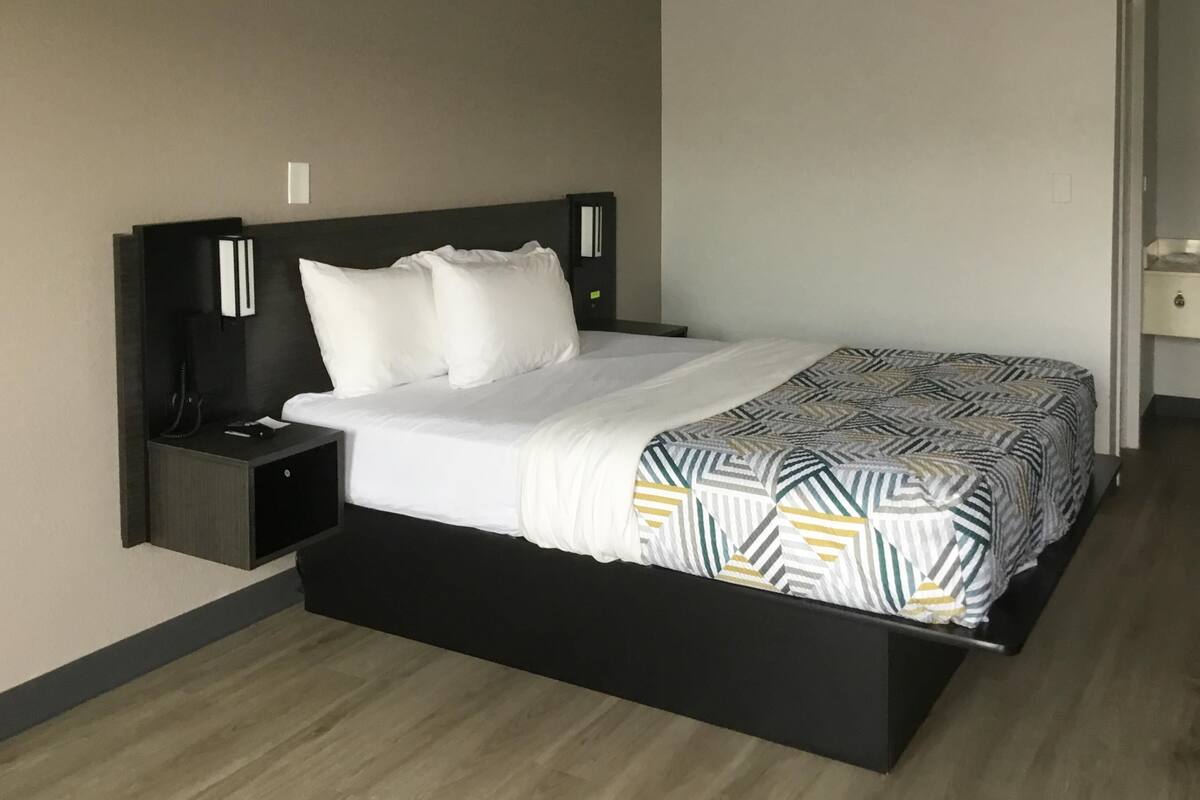 A modern hotel room with a large bed, a bedside table, and a nightstand.