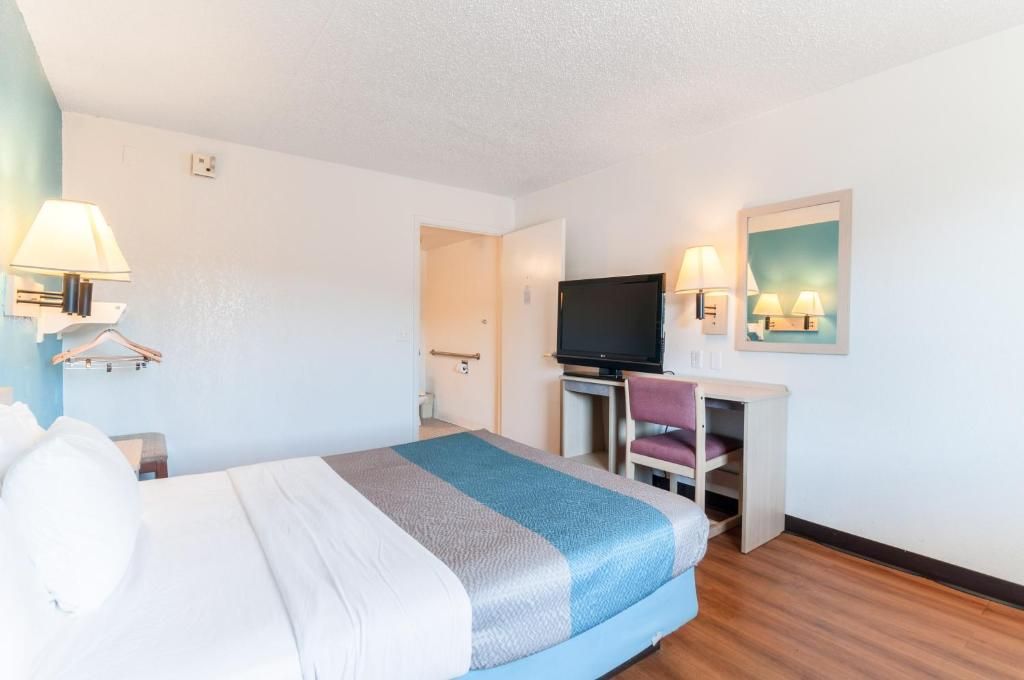 A hotel room with a bed, a desk, a television, and wall-mounted lamps.