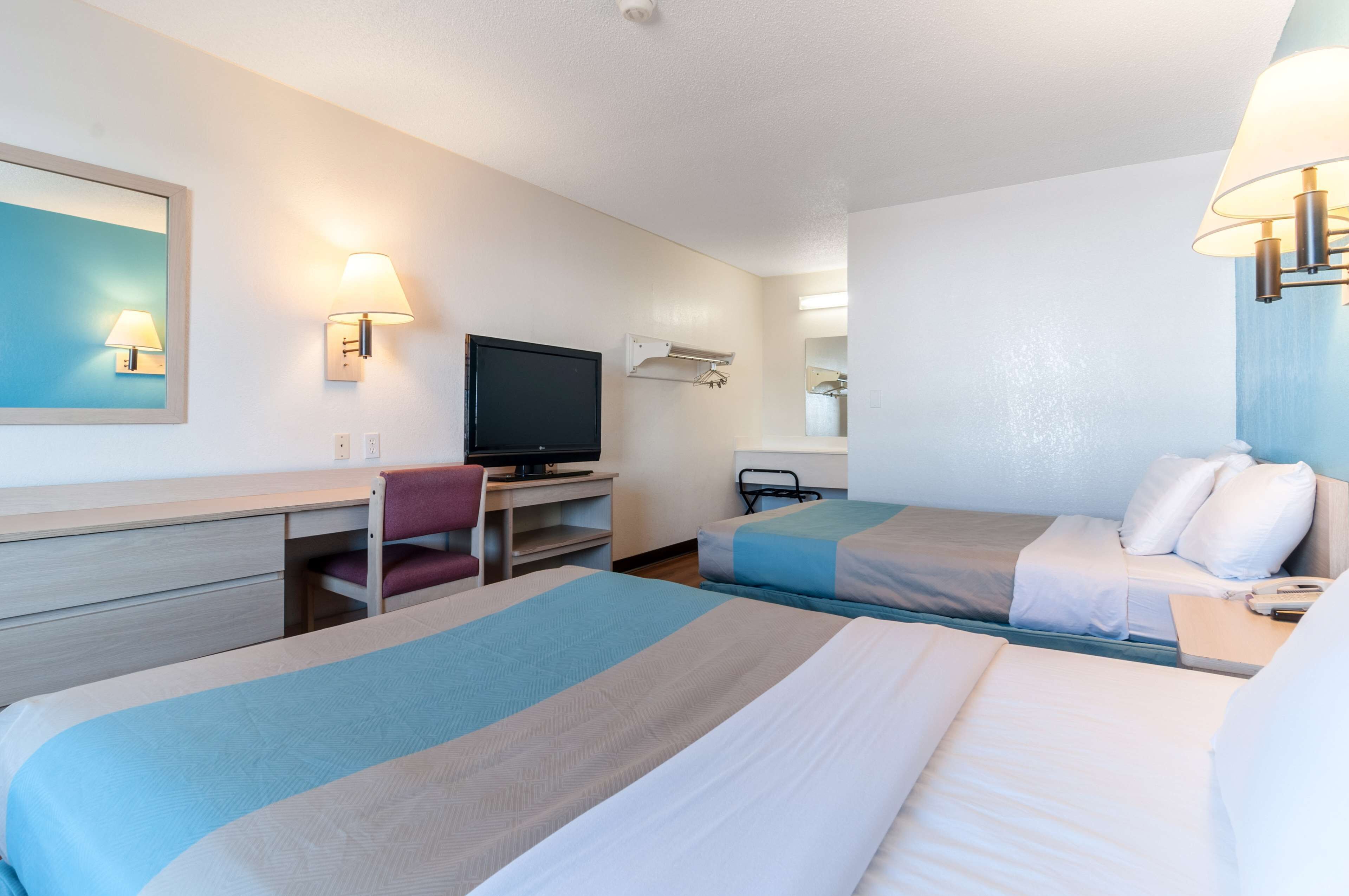 A hotel room with two beds, a desk, a chair, a television, and a mirror.