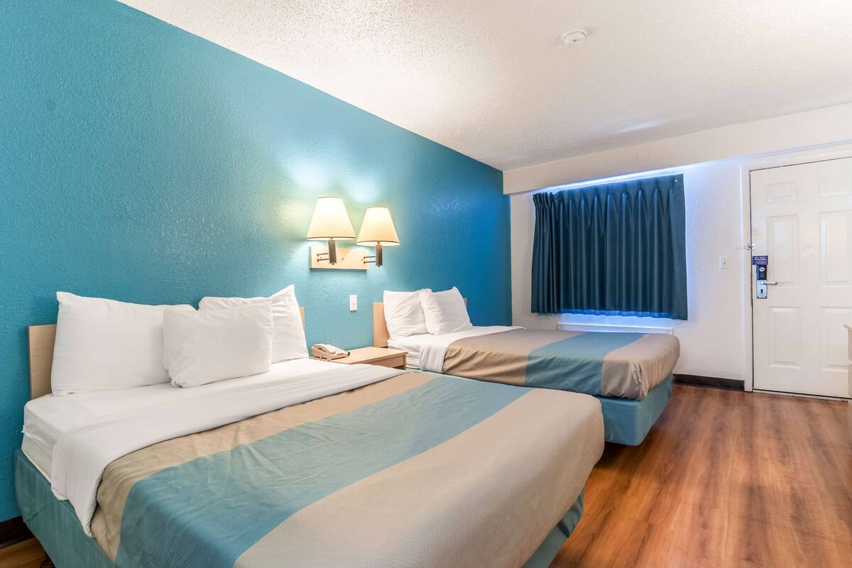 A hotel room with two beds, a nightstand, a telephone, and a window with curtains.