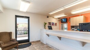 Ein Empfangsbereich mit einer Rezeption, einem Sessel, einer Tür zum Außenbereich und einem an der Wand befestigten Fernseher.