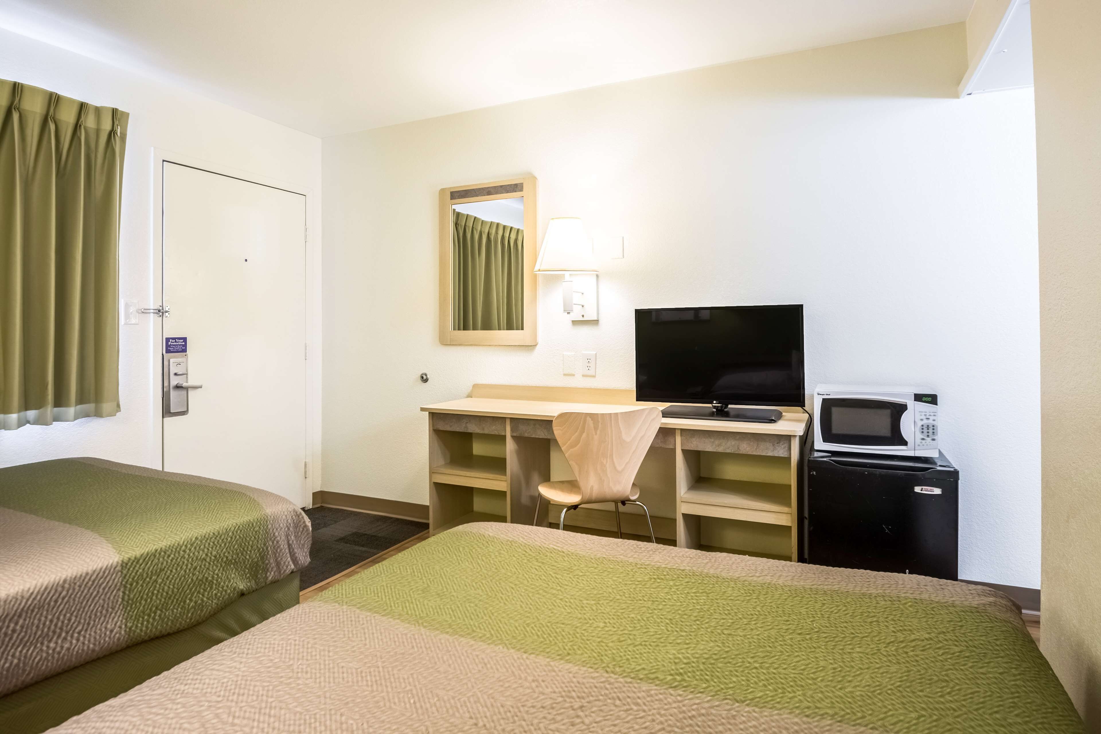 A hotel room with two beds, a desk with a chair, a television, a microwave, and a mirror.