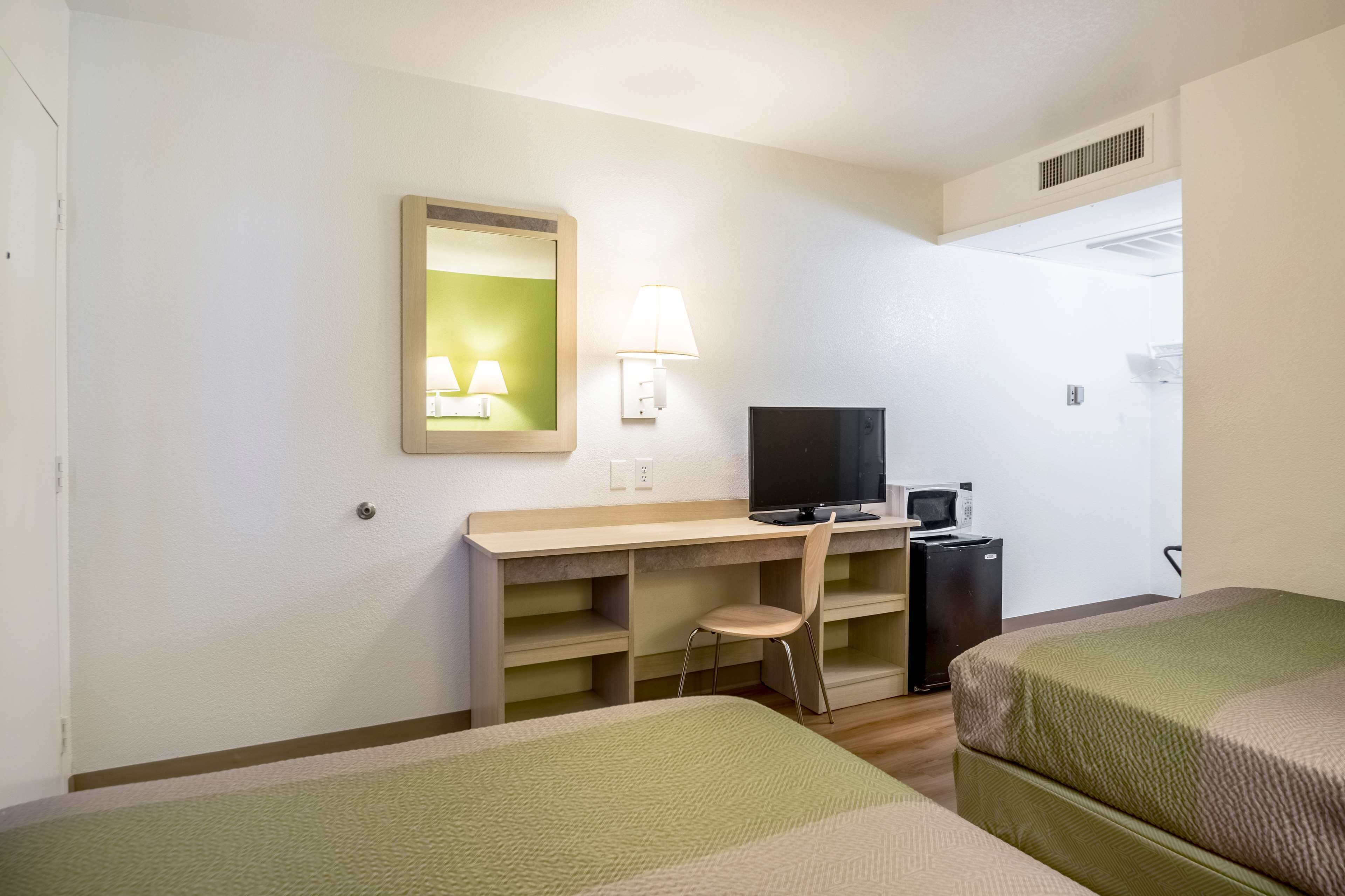 Une chambre d’hôtel équipée d’un lit, d’un bureau avec une chaise, d’une télévision, d’un four à micro-ondes et d’un petit réfrigérateur.