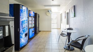 A corridor with vending machines, a small table with chairs, and a door leading to another area. - Motel 6 Pueblo, CO - I-25 (Pueblo)