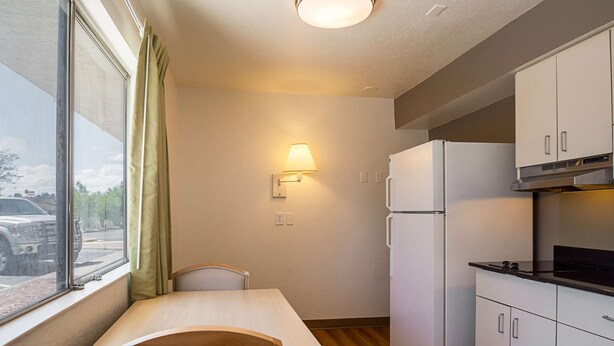 A compact kitchen with a dining table, a refrigerator, and a wall-mounted lamp. - Motel 6 Pueblo, CO - I-25 (Pueblo)