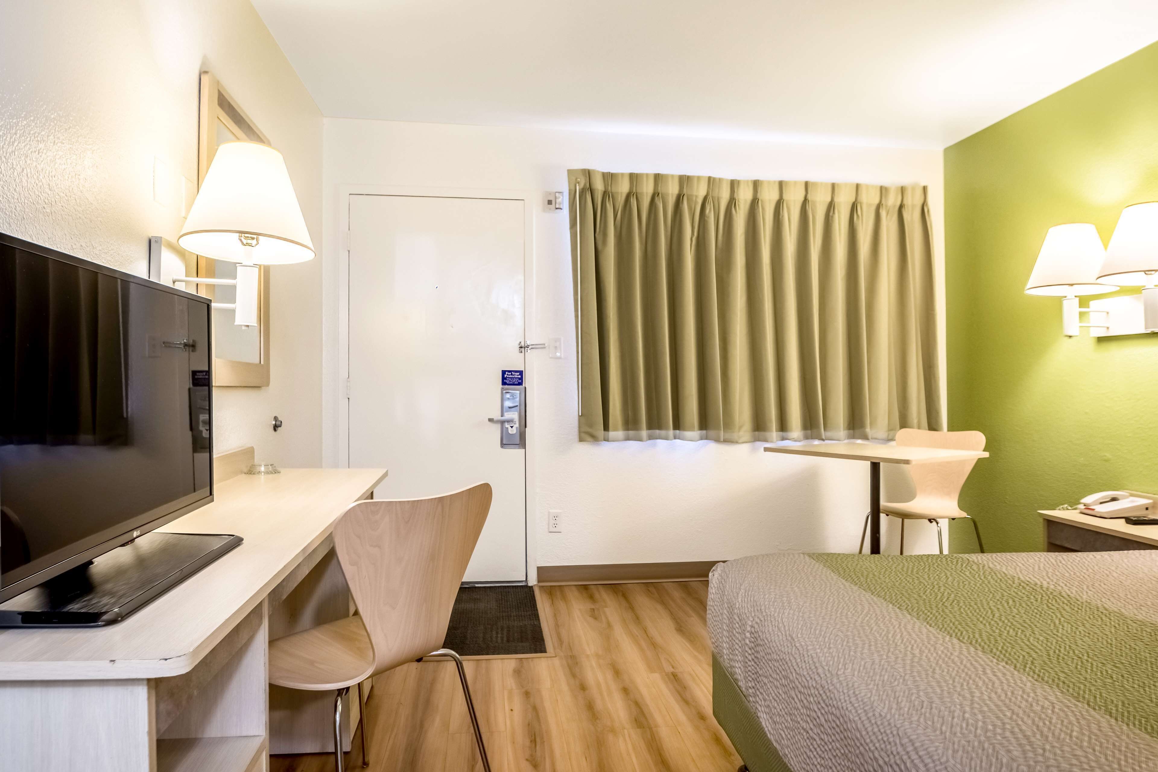 A hotel room with a bed, desk, chair, television, and two lamps.