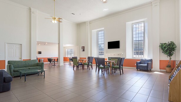 A spacious room with a green sofa, multiple chairs, a coffee table, and a television mounted on the wall. - Motel 6 Williams, AZ - West - Grand Canyon (Williams)