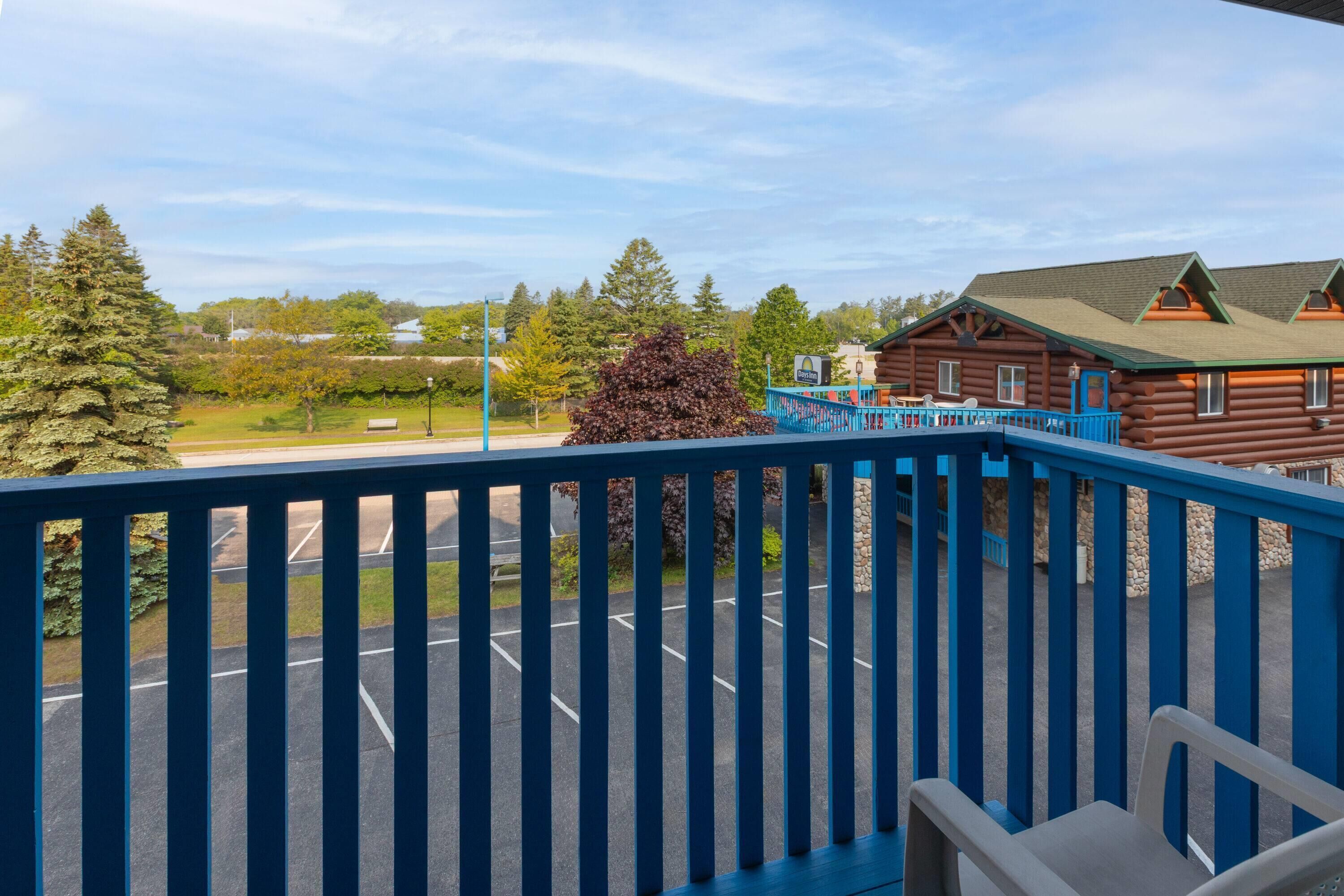 Une cabane en bois avec un balcon bleu, un parking et une vue sur des arbres et un lac.