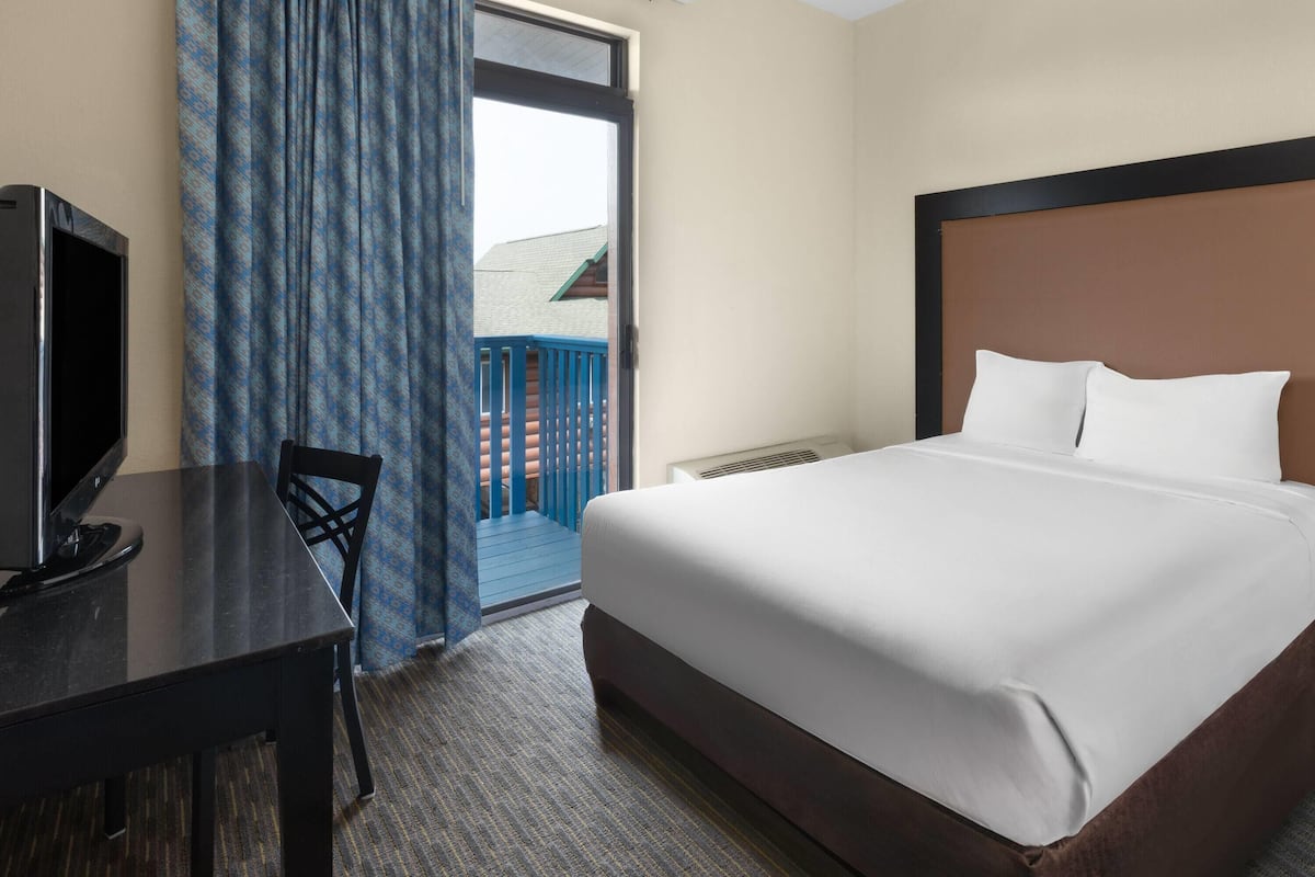 Habitación de hotel con cama, escritorio con televisor y vista a un balcón con barandilla azul.