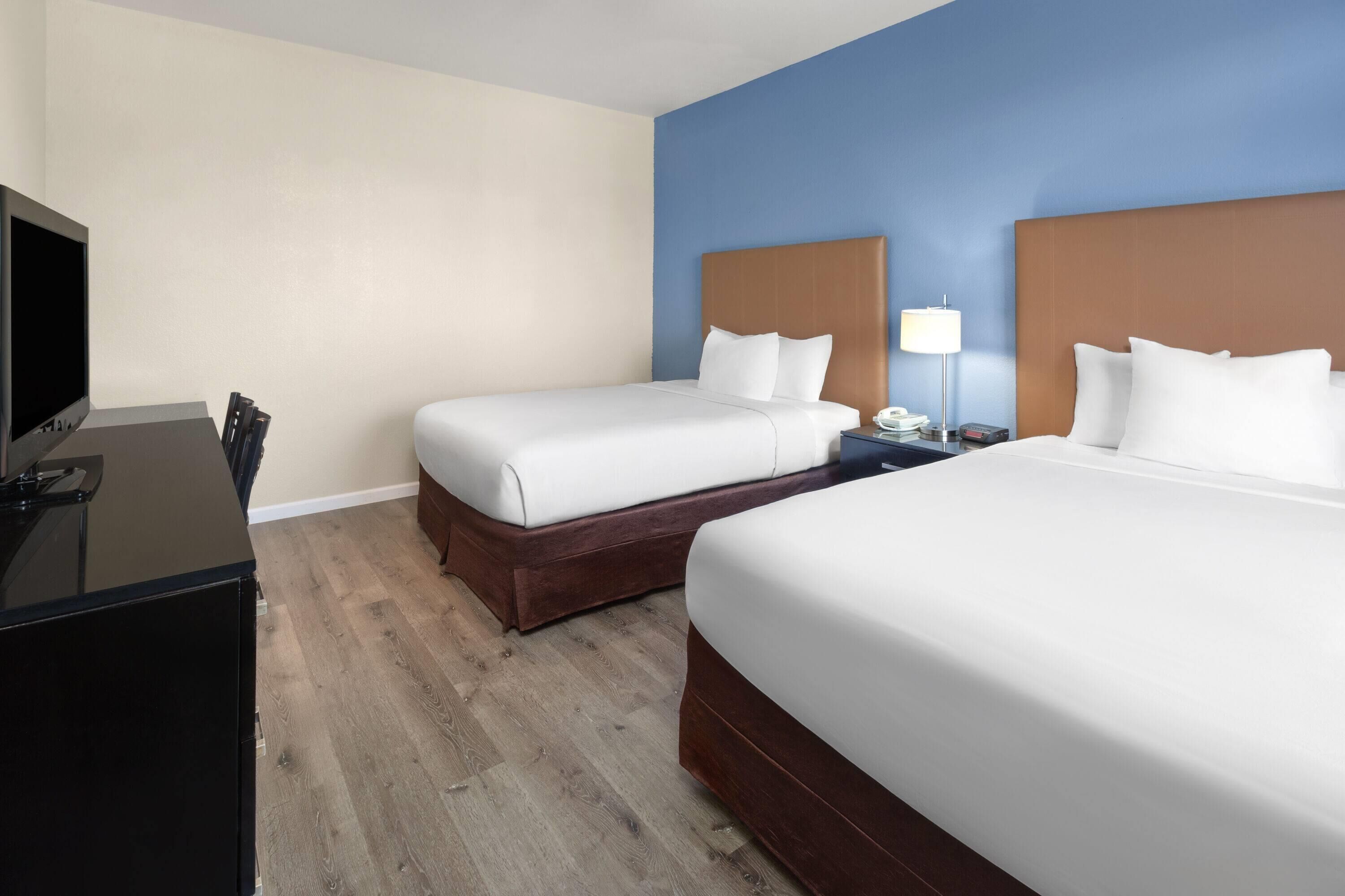 A hotel room with two beds, a desk, and a TV.