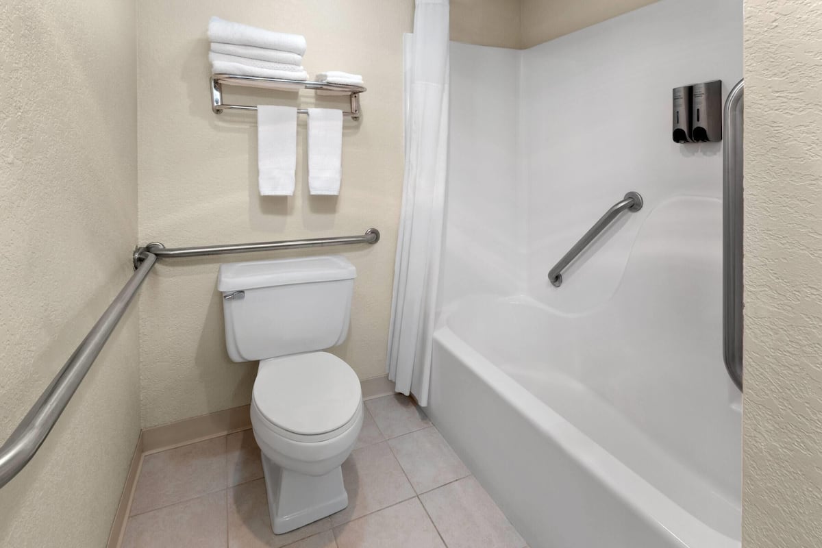 Un baño con inodoro, bañera, ducha y barra de apoyo.