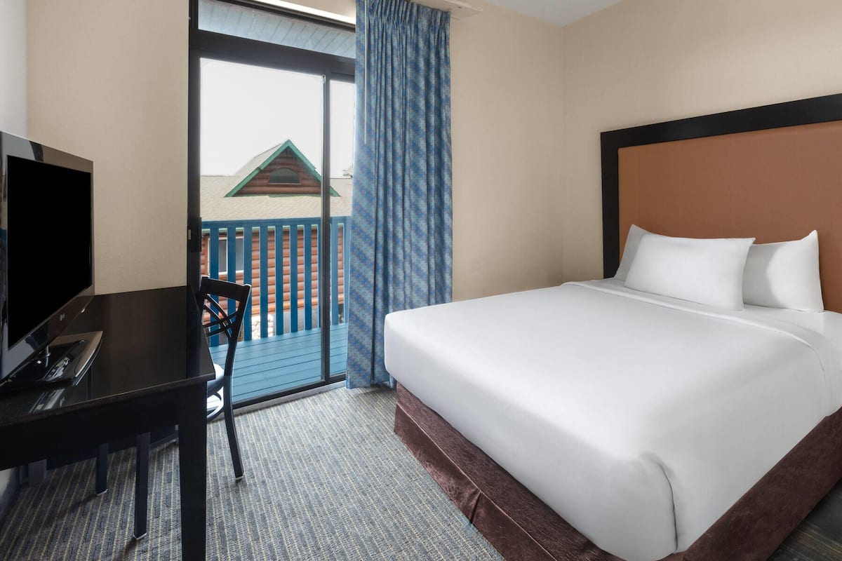 Habitación de hotel con cama, escritorio con computadora y vista a un balcón con cerca de madera.